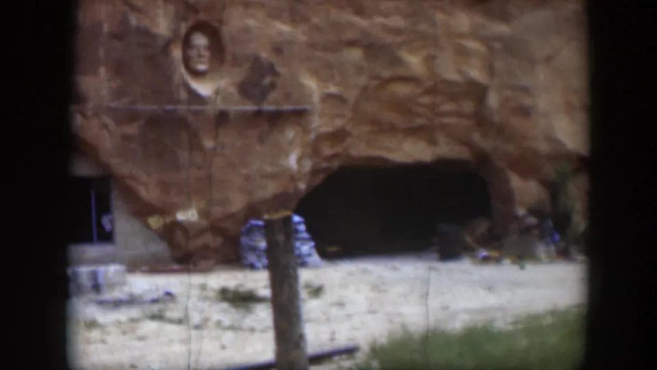 1951 Utah home-movie frame of sandstone with a carved face above a cave-like recess and rough stonework nearby.