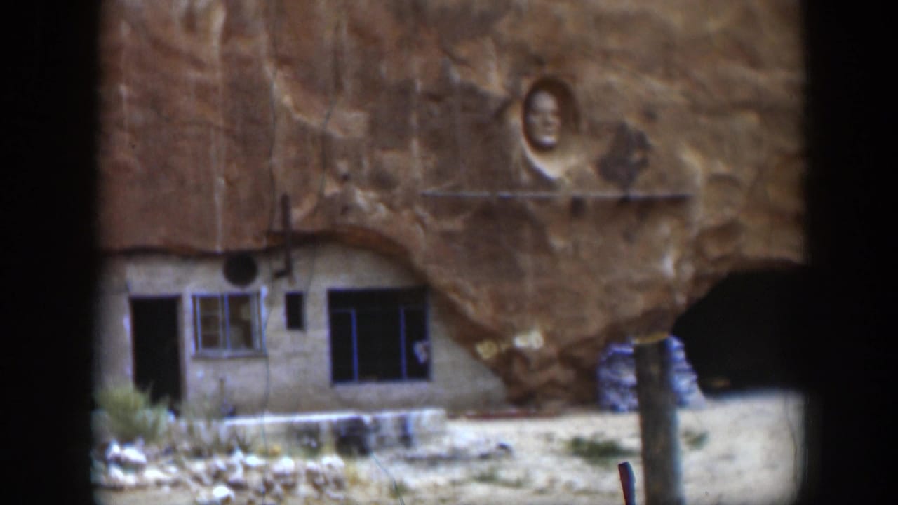 1951 Utah 8mm frame of the rock-side structure, with windows, a dark doorway, carved face, and cave-like opening.