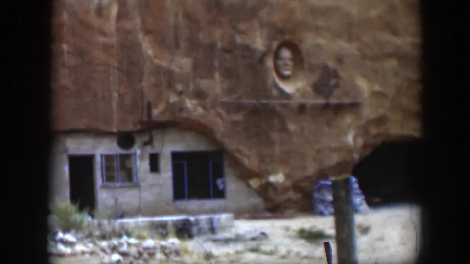 1951 Utah 8mm frame of the rock-side structure, with windows, a dark doorway, carved face, and cave-like opening.