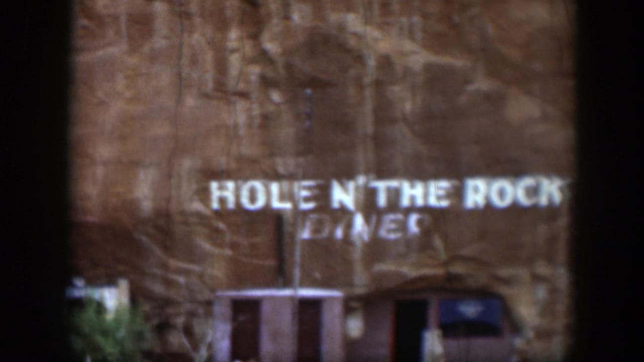 1951 Utah home-movie frame showing the diner lettering on the rock face, with the entrance and sparse vegetation below.