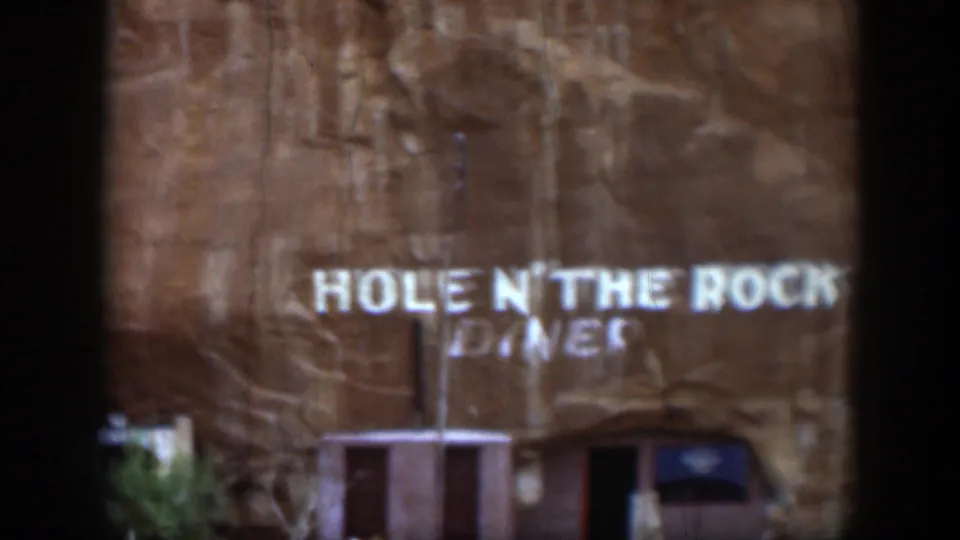 1951 Utah home-movie frame showing the diner lettering on the rock face, with the entrance and sparse vegetation below.