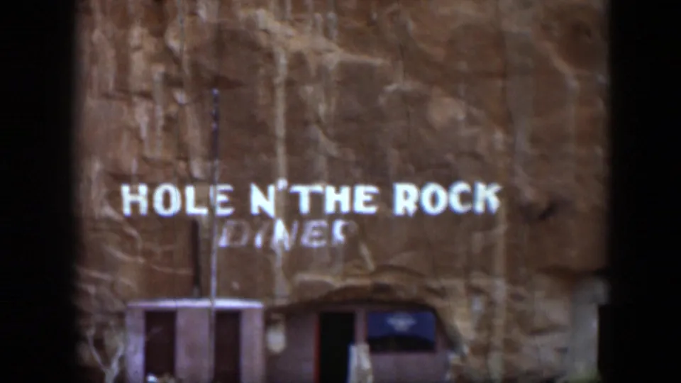 1951 Utah home-movie frame showing the Hole N' The Rock Diner sign painted on a sandstone cliff face.