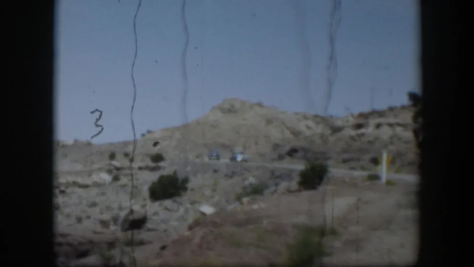 1951 Utah road-travel frame showing arid hills, sparse brush, distant vehicles, and dark vehicle-window borders.