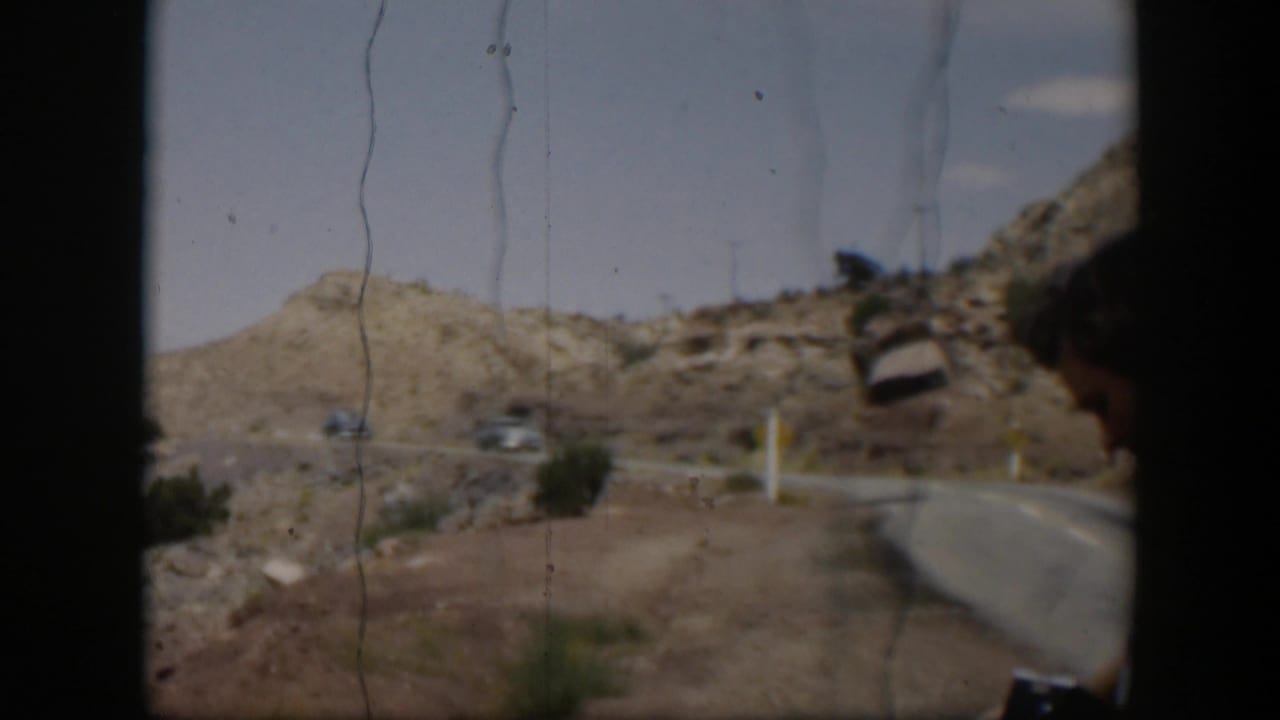 1951 Utah desert road scene with two distant cars, arid hills, sparse vegetation, and dark 8mm frame edges.
