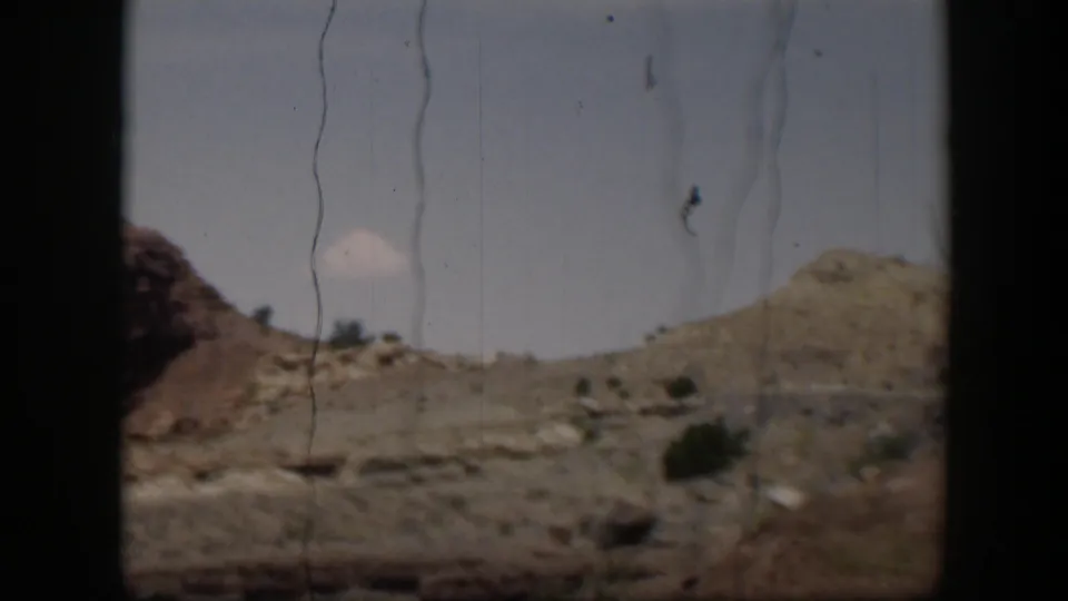 A 1951 Utah desert roadside view with rocky hills, sparse shrubs, pale sky, and prominent 8mm scratches and frame borders.