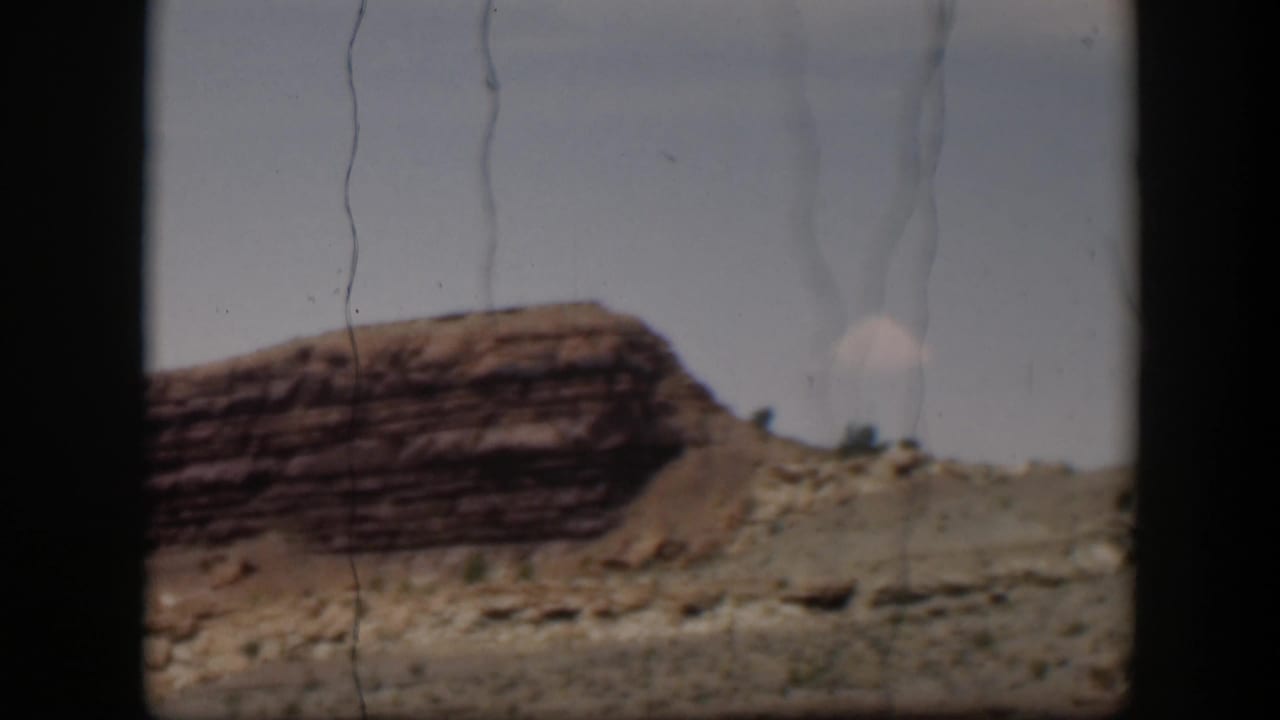 1951 Utah frame with a red-brown layered outcrop, dry slope, small shrubs, and visible film scratches under a pale sky.