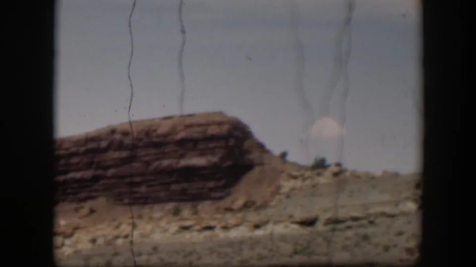 1951 Utah frame with a red-brown layered outcrop, dry slope, small shrubs, and visible film scratches under a pale sky.
