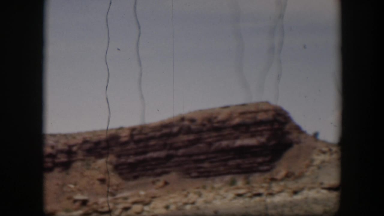 1951 Utah home-movie still showing a low layered ridge, rocky foreground, sparse vegetation, and aged 8mm film marks.