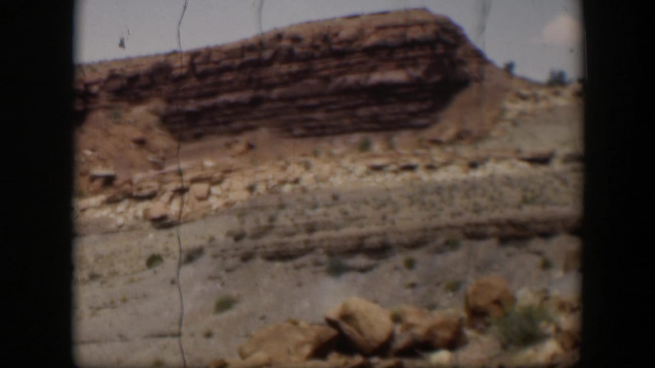 1951 Utah frame showing a closer layered red rock formation, boulders, dry wash-like ground, scrub, and film gate borders.