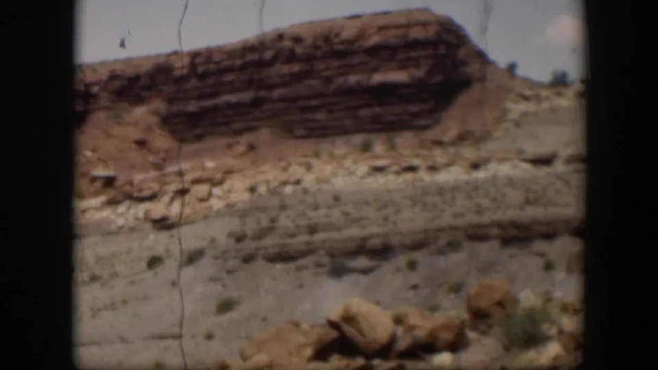 1951 Utah frame showing a closer layered red rock formation, boulders, dry wash-like ground, scrub, and film gate borders.