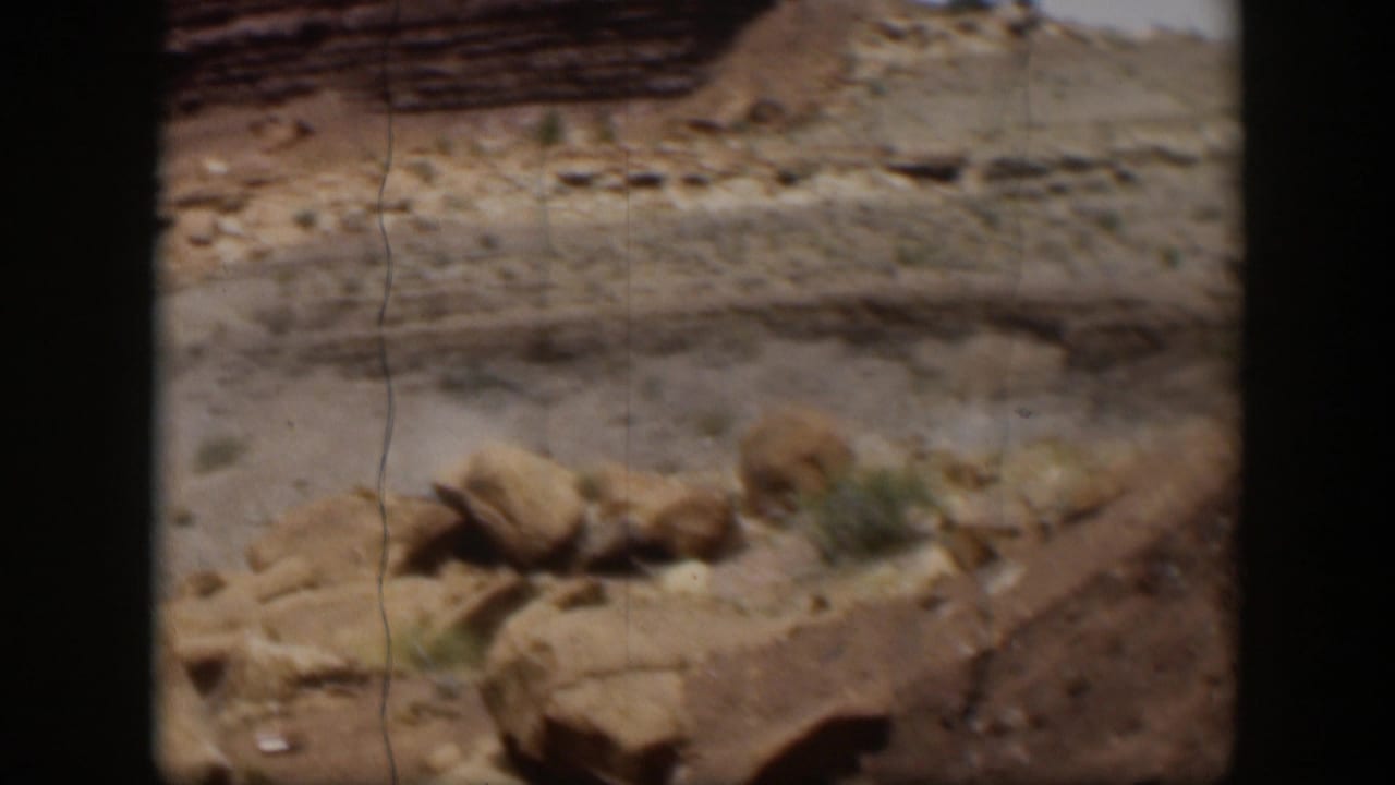 1951 Utah 8mm view of arid terrain with horizontal rock layers, scattered boulders, and sparse scrub.