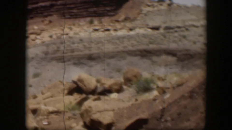 1951 Utah 8mm view of arid terrain with horizontal rock layers, scattered boulders, and sparse scrub.