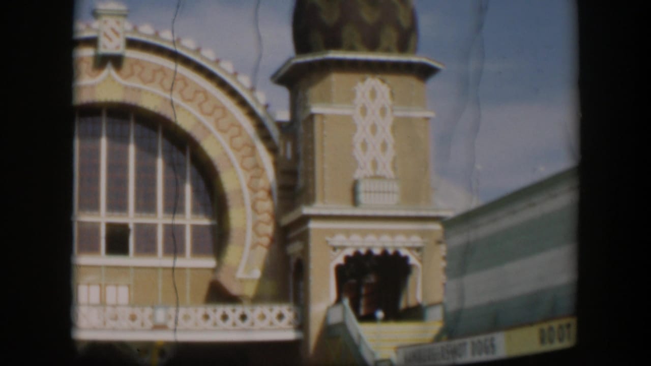 1951 Utah home-movie frame with a large arched window, white decorative trim, domed tower, balcony rail, and partial root beer sign.