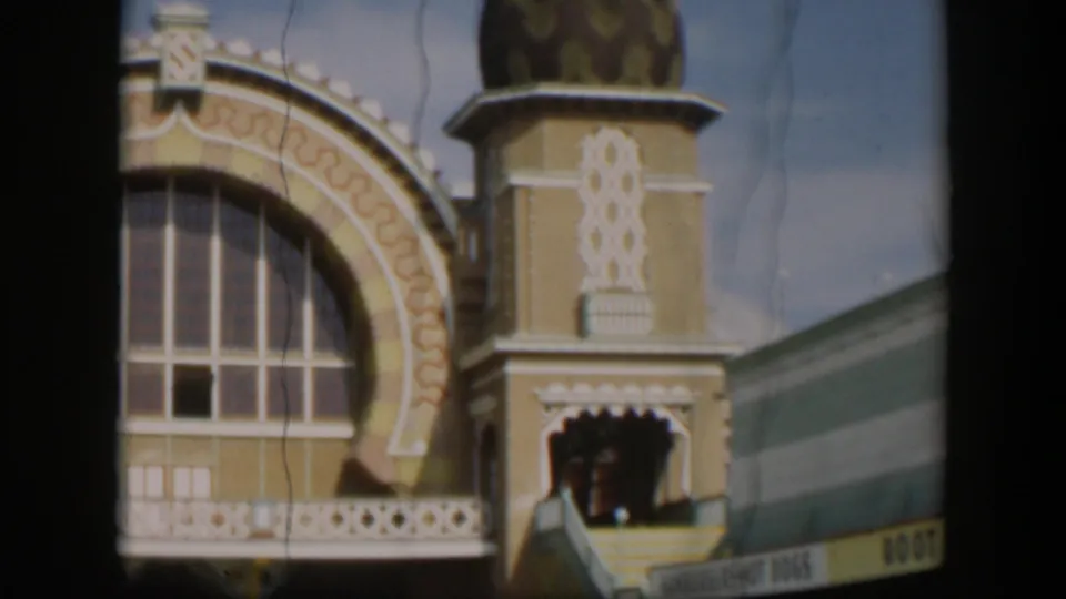 1951 Utah home-movie frame with a large arched window, white decorative trim, domed tower, balcony rail, and partial root beer sign.