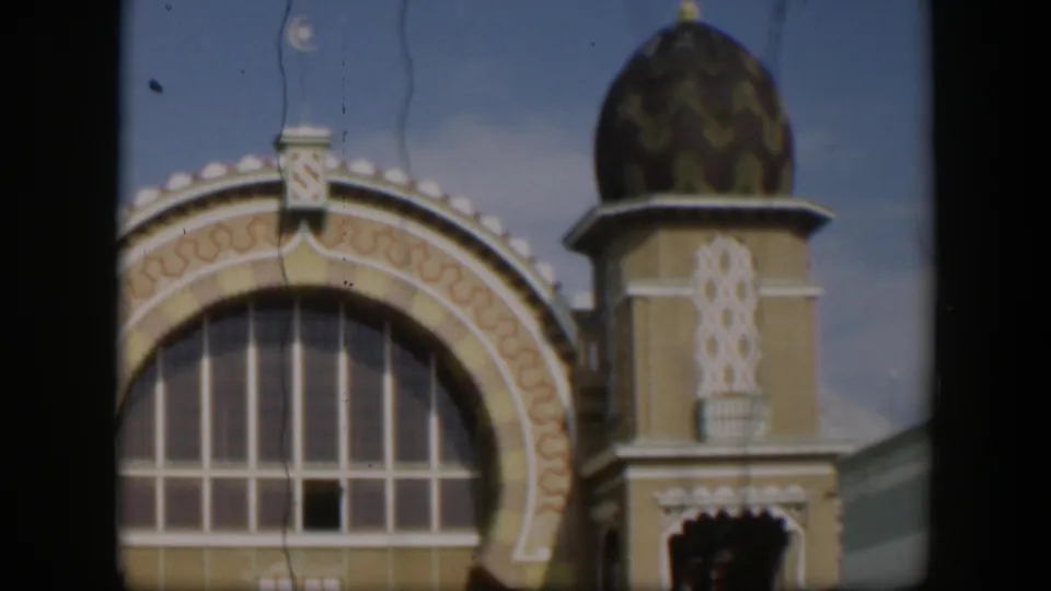 1951 Utah 8mm frame centered on an ornate yellow-and-cream facade with a large arched window, patterned trim, and domed tower.