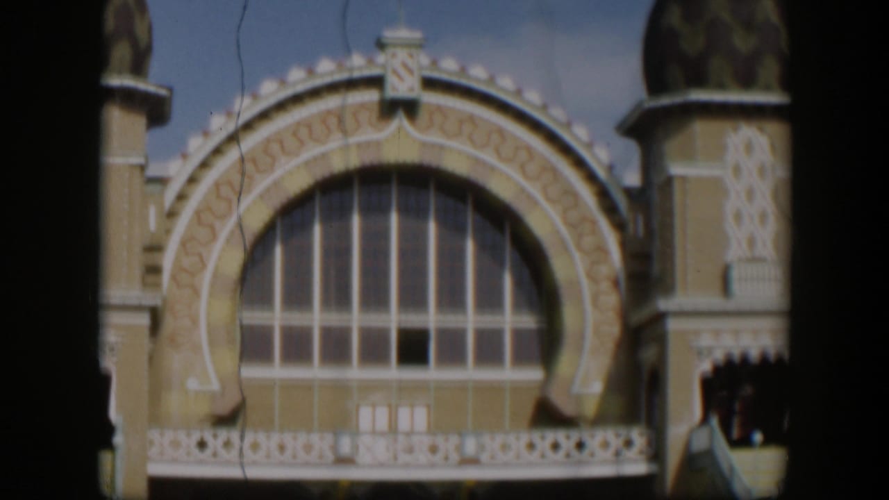 1951 Utah home-movie frame showing an ornate arched window, balcony railing, domed tower, decorative facade, and partial food-stand entrance.