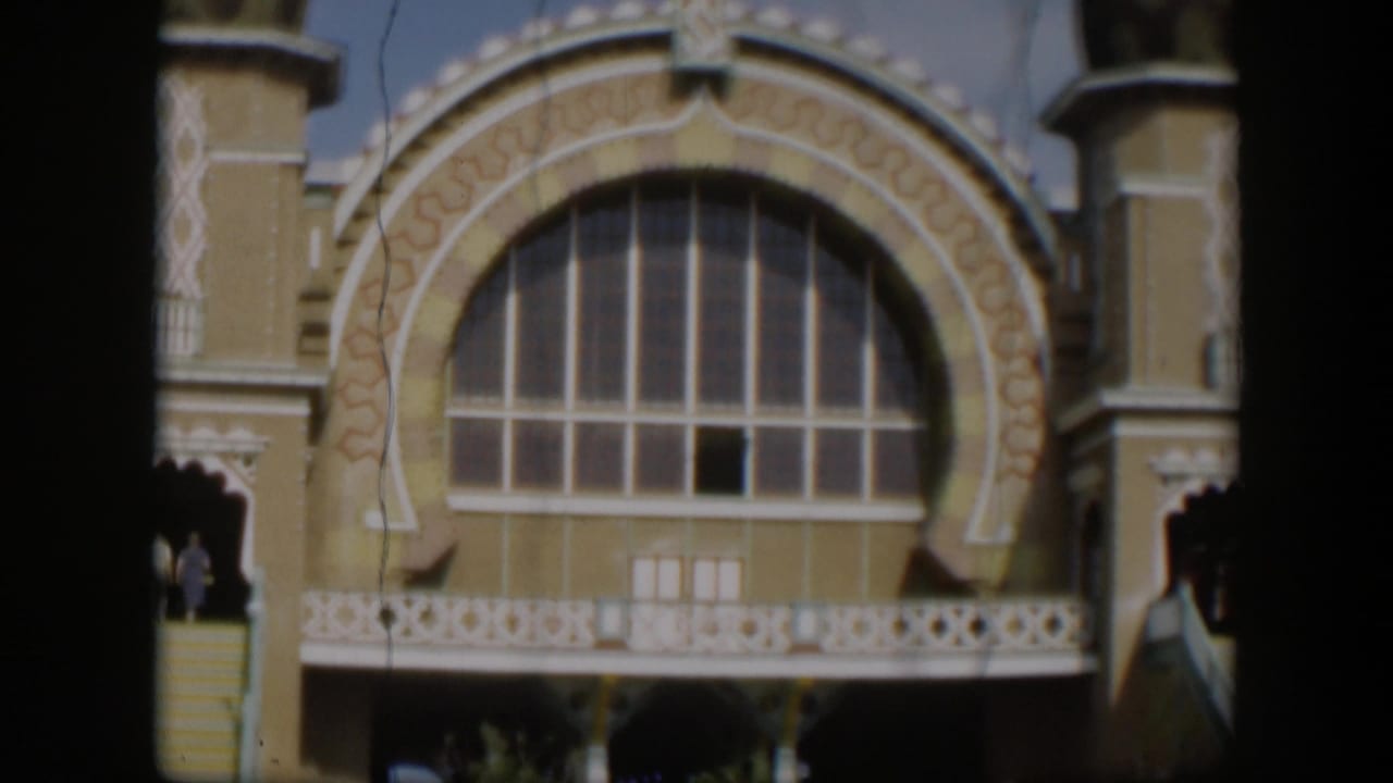 Tan ornate building facade with a large arched window and exterior stairs in sunlight.