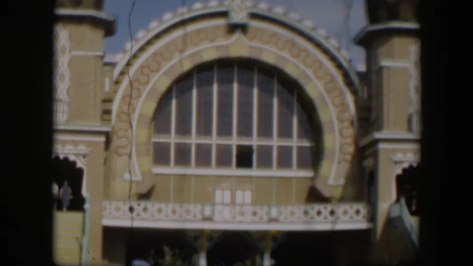 1951 Utah 8mm frame showing a tan ornate facade with a large arched window, white trim, and shadowed stair openings.