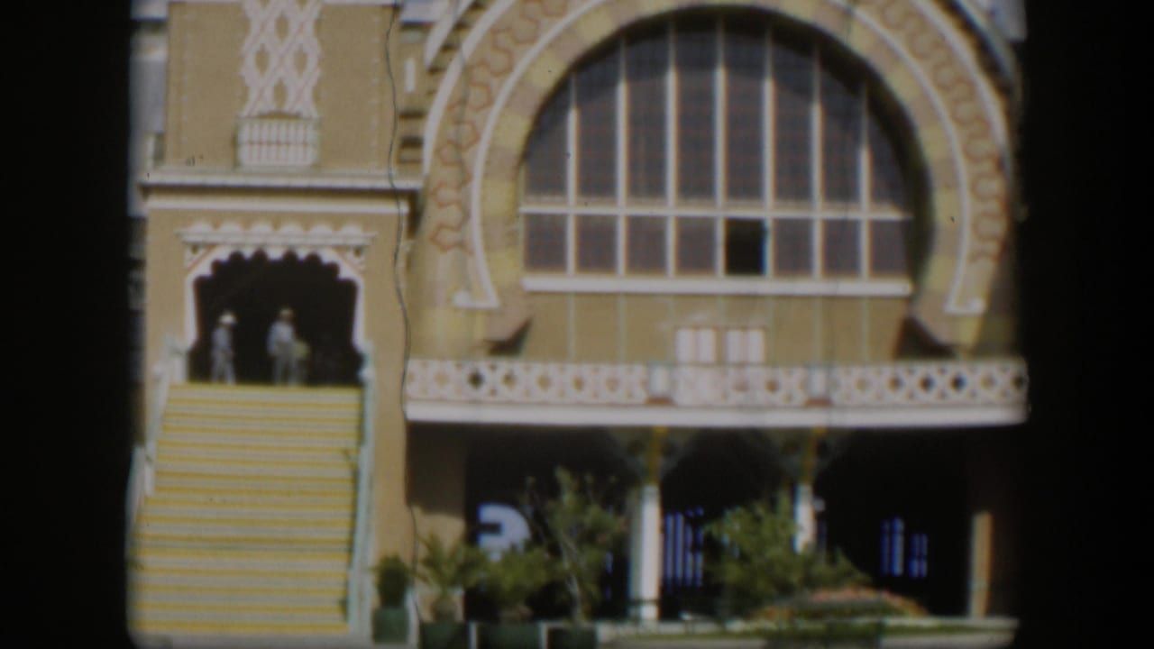 1951 Utah 8mm frame showing two distant people on exterior stairs near an ornate tan facade with a large arched window.