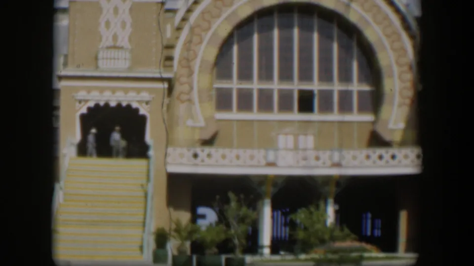 1951 Utah 8mm frame showing two distant people on exterior stairs near an ornate tan facade with a large arched window.