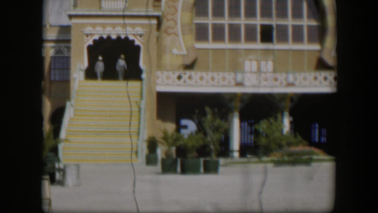 1951 Utah 8mm frame showing a yellow decorative building facade, white trim, broad stairs, and two distant figures near the entrance.