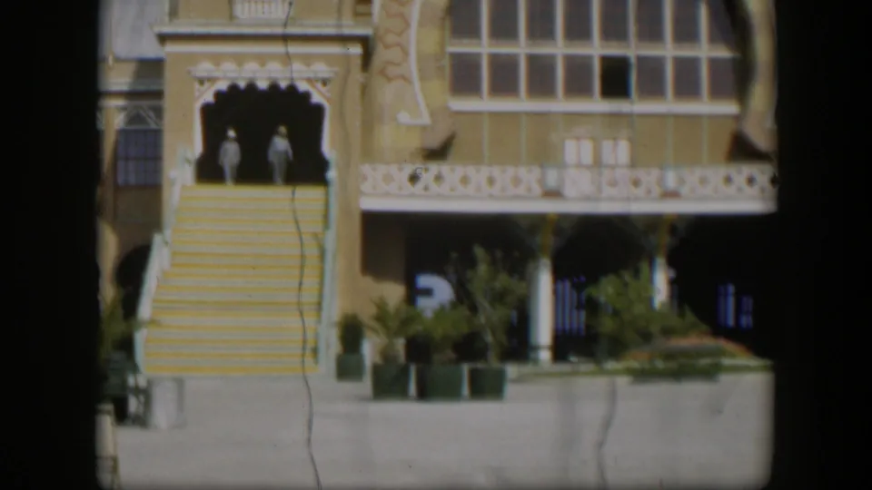 1951 Utah 8mm frame showing a yellow decorative building facade, white trim, broad stairs, and two distant figures near the entrance.