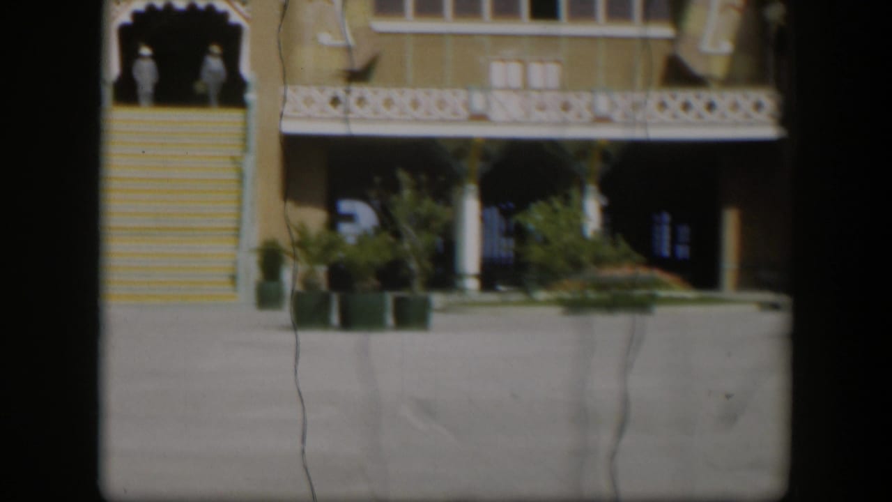 1951 Utah exterior frame with a yellow building, white ornamental trim, broad stairs, potted plants, and two distant people by the entrance.