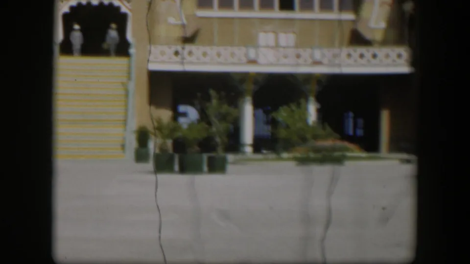 1951 Utah exterior frame with a yellow building, white ornamental trim, broad stairs, potted plants, and two distant people by the entrance.