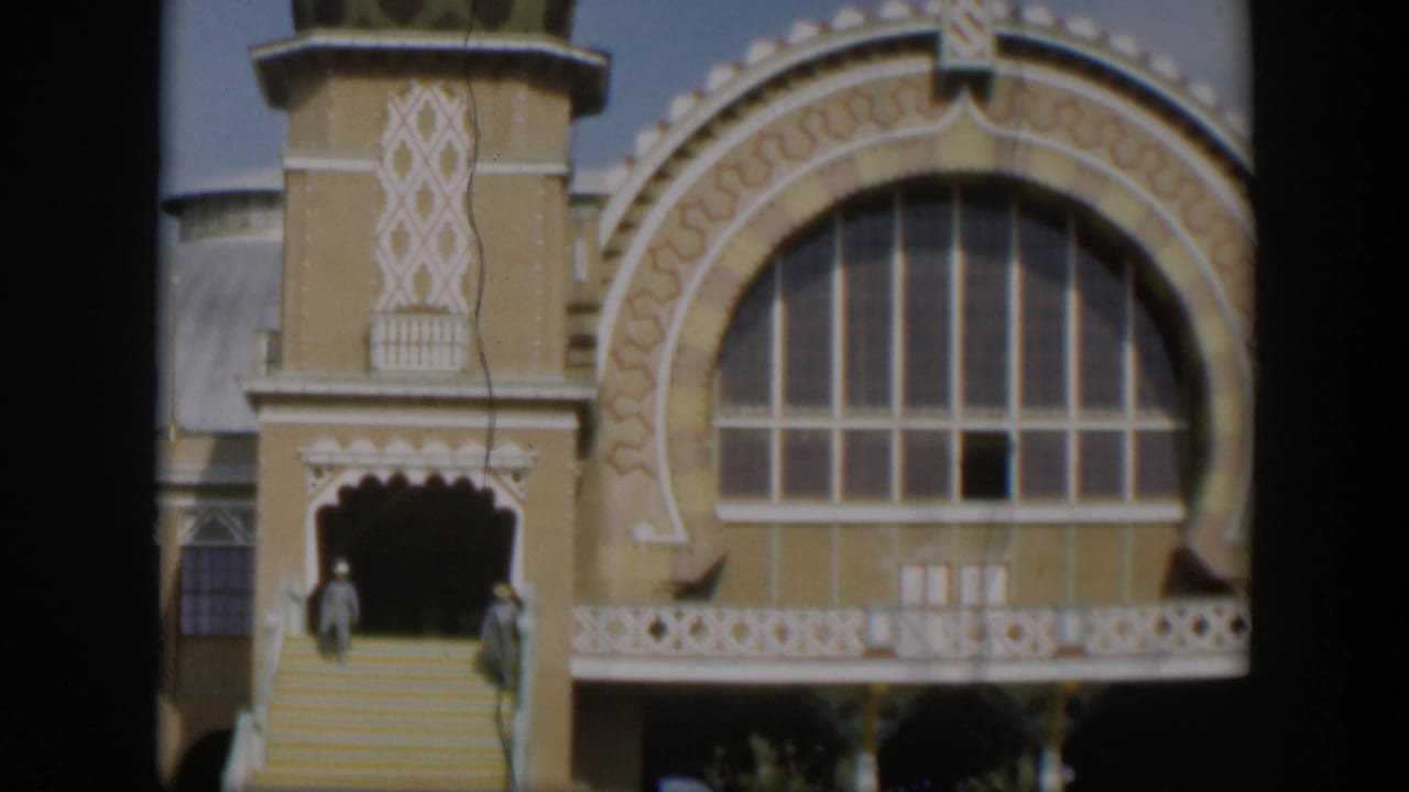 1951 Utah 8mm frame showing an ornate religious building facade with a large arched window, patterned trim, steps, and distant visitors.