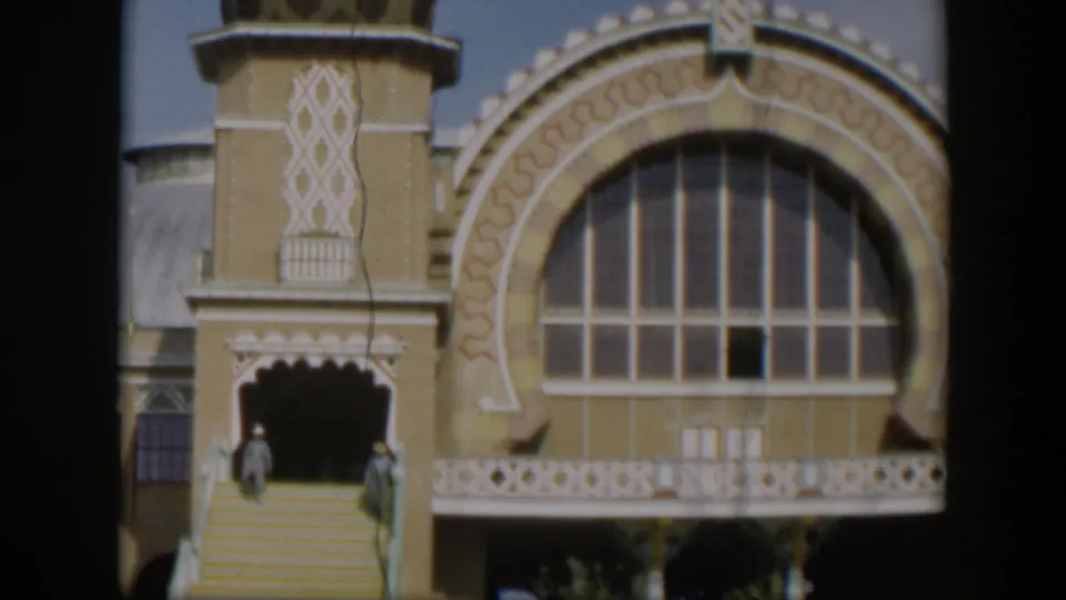 1951 Utah 8mm frame showing an ornate religious building facade with a large arched window, patterned trim, steps, and distant visitors.