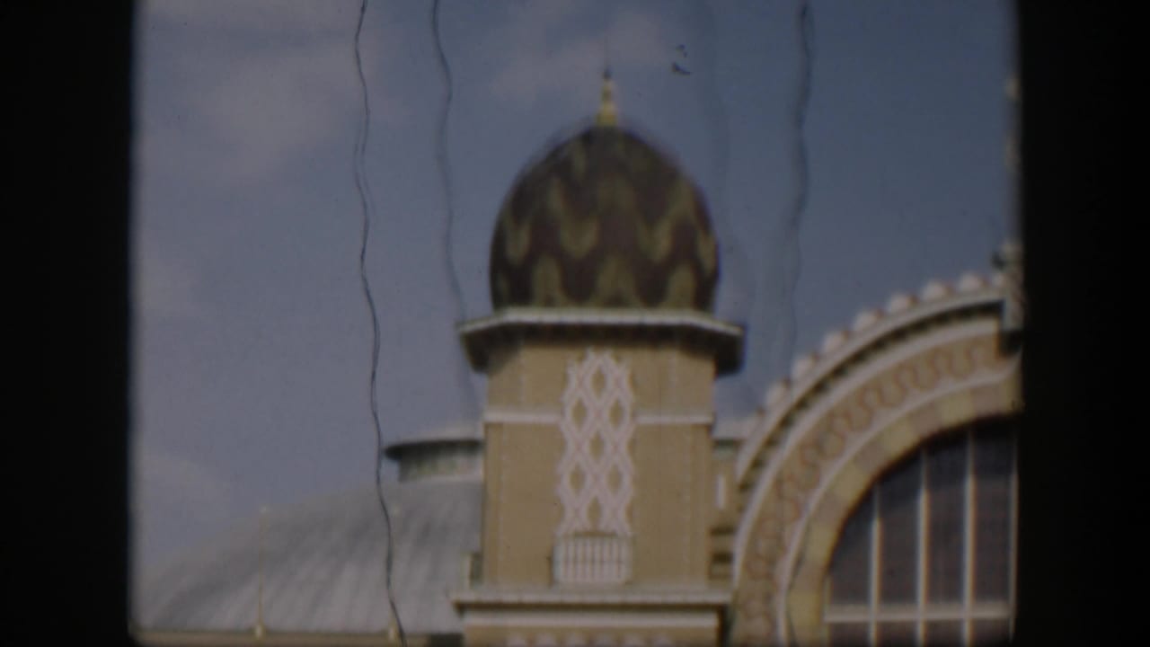1951 Utah 8mm frame with a patterned dome, tan tower, curved roof, and ornate arched window partially divided by dark foreground framing.