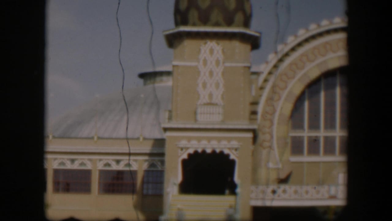 1951 Utah 8mm frame tilting down to the lower facade, showing a scalloped doorway, steps, railings, windows, and ornate arch decoration.