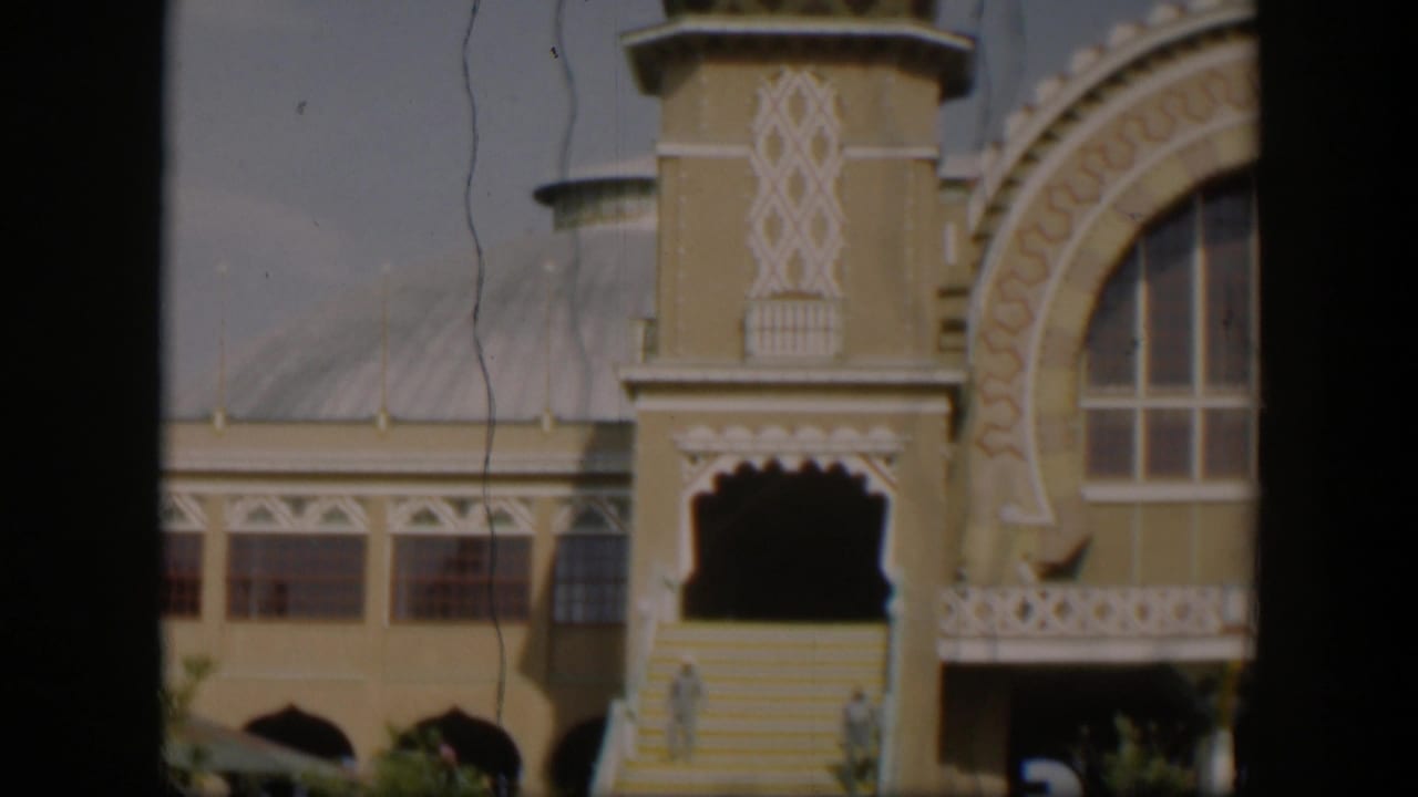 1951 Utah 8mm frame showing the ornate entrance, steps, railing, arched window, and small indistinct people near the lower doorway.