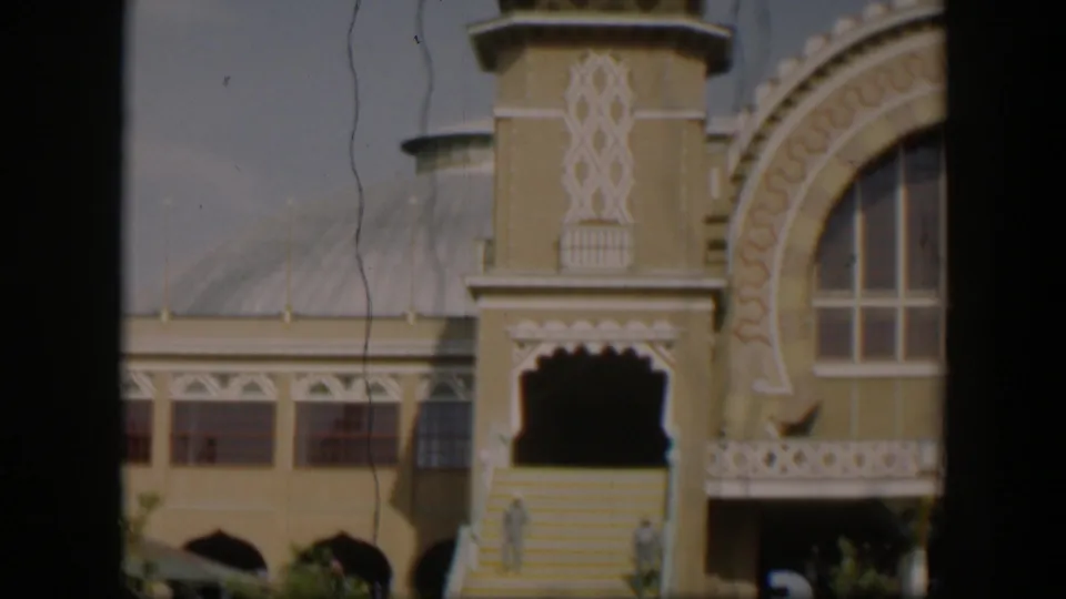 1951 Utah 8mm frame showing the ornate entrance, steps, railing, arched window, and small indistinct people near the lower doorway.