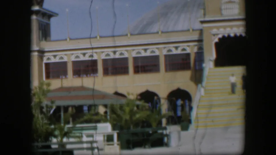 1951 Utah home-movie frame showing the resort courtyard from a closer angle, with striped steps, arches, benches and plants in bright sun.