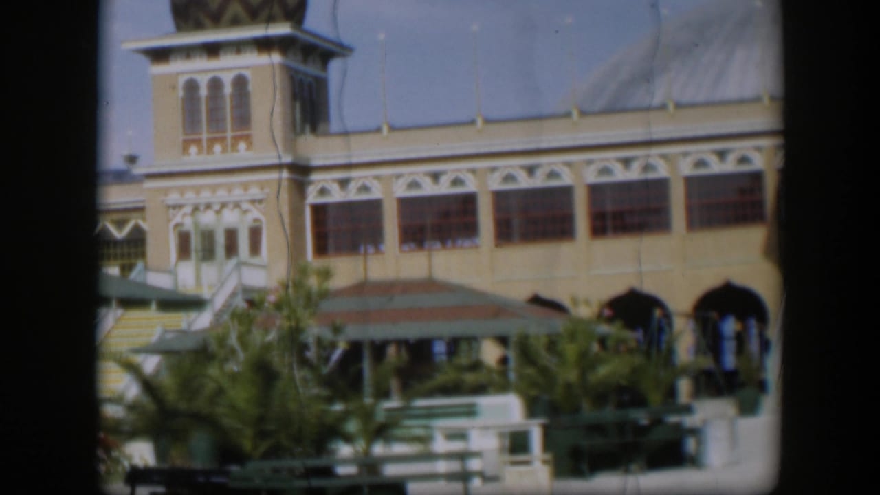 1951 Utah frame with a wider view of the resort facade, tower detail, arched windows, umbrella shade, benches and courtyard greenery.