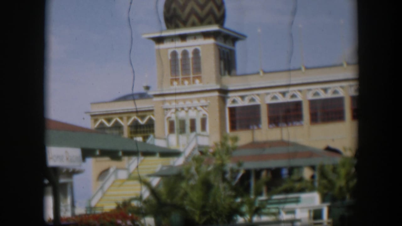 Utah-labeled 1951 home-movie frame of the towered building from outside, with arched windows, a patterned dome, pavilion roof, and greenery.