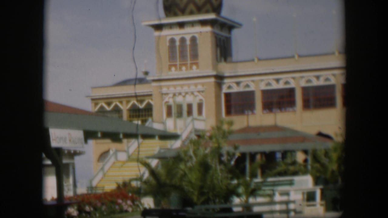 1951 Utah home-movie frame of the yellow facade and domed tower, with exterior stairs, green awnings, landscaping, and railings in front.