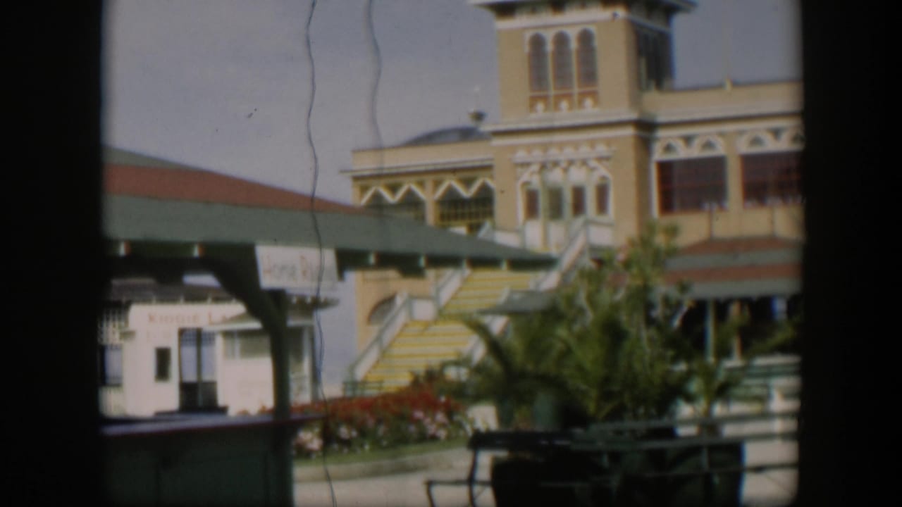 1951 Utah 8mm frame with the yellow building partly cropped, showing the stairway, green awning, landscaped plants, and partial sign text.