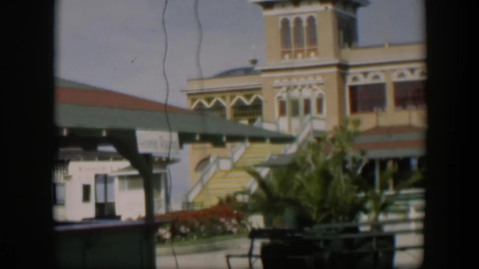 1951 Utah 8mm frame with the yellow building partly cropped, showing the stairway, green awning, landscaped plants, and partial sign text.