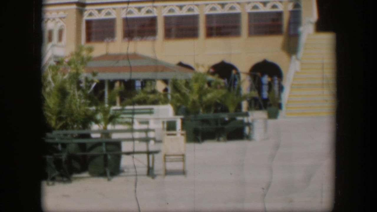 1951 Utah exterior showing a resort courtyard, green benches, potted palms, arched entryways, and yellow striped stairs.