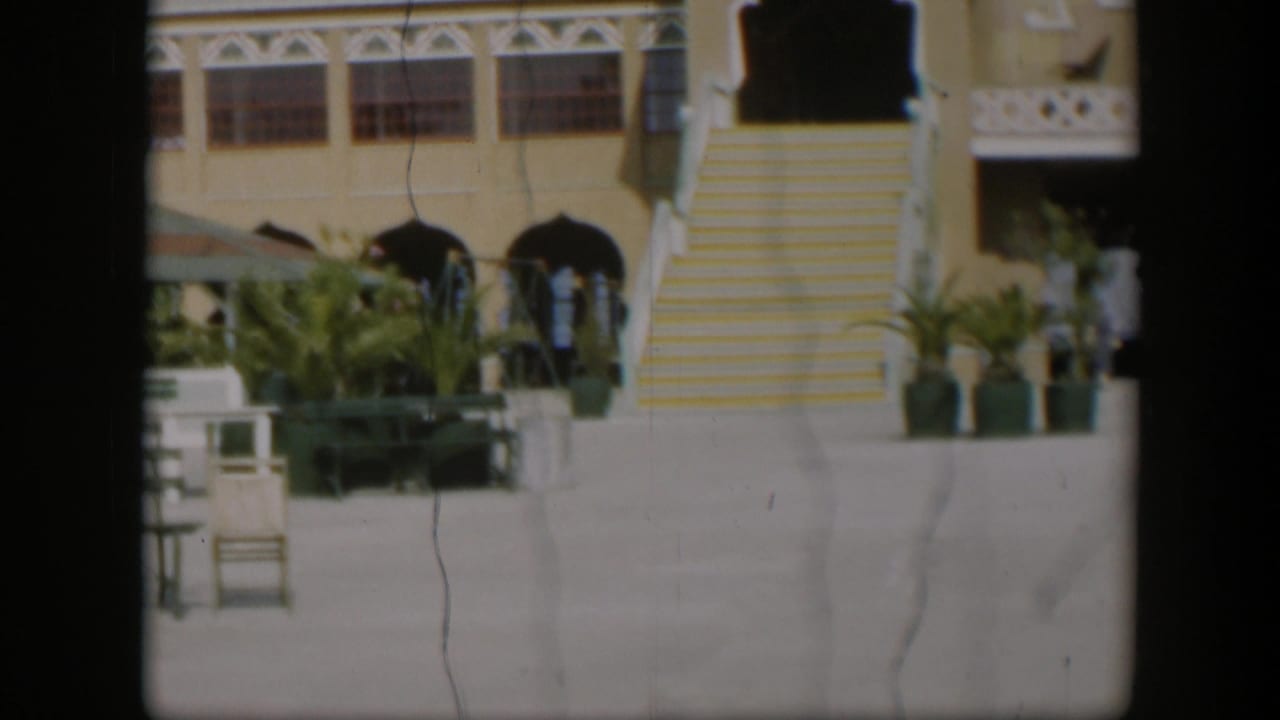 1951 Utah resort view with a prominent yellow striped staircase, arched openings, palms, benches, and distant people.
