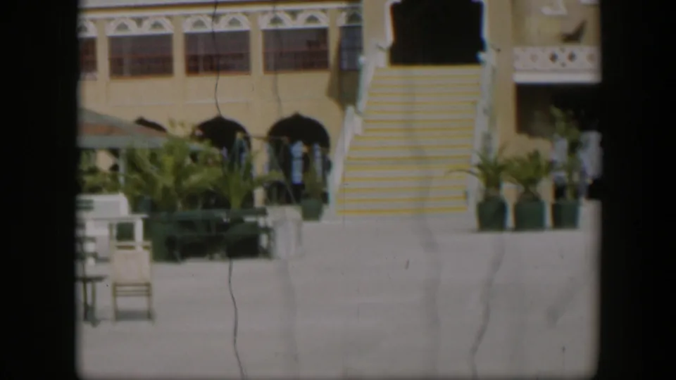 1951 Utah resort view with a prominent yellow striped staircase, arched openings, palms, benches, and distant people.