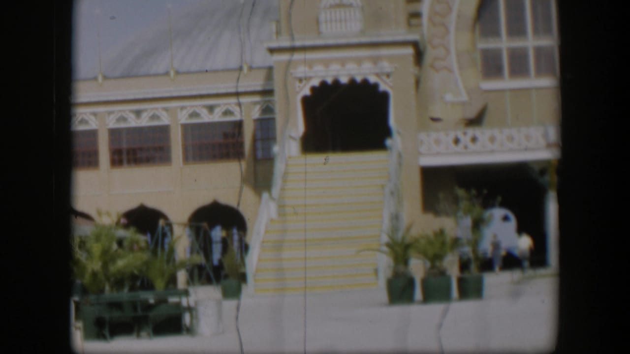 1951 Utah 8mm frame with a closer visitor view of the Salt Lake Tabernacle entrance, steps, palms, balcony, and distant people.