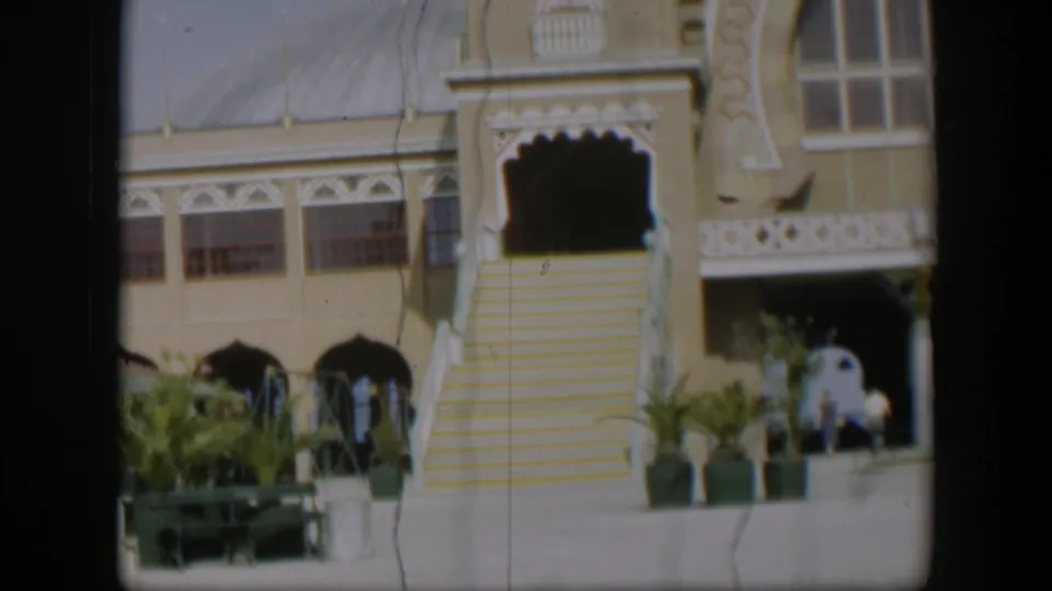 1951 Utah 8mm frame with a closer visitor view of the Salt Lake Tabernacle entrance, steps, palms, balcony, and distant people.