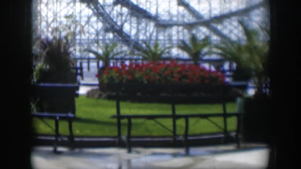 1951 Utah 8mm frame showing a landscaped garden near the Salt Lake Tabernacle, with red flowers, lawn, benches, and glasshouse structure.