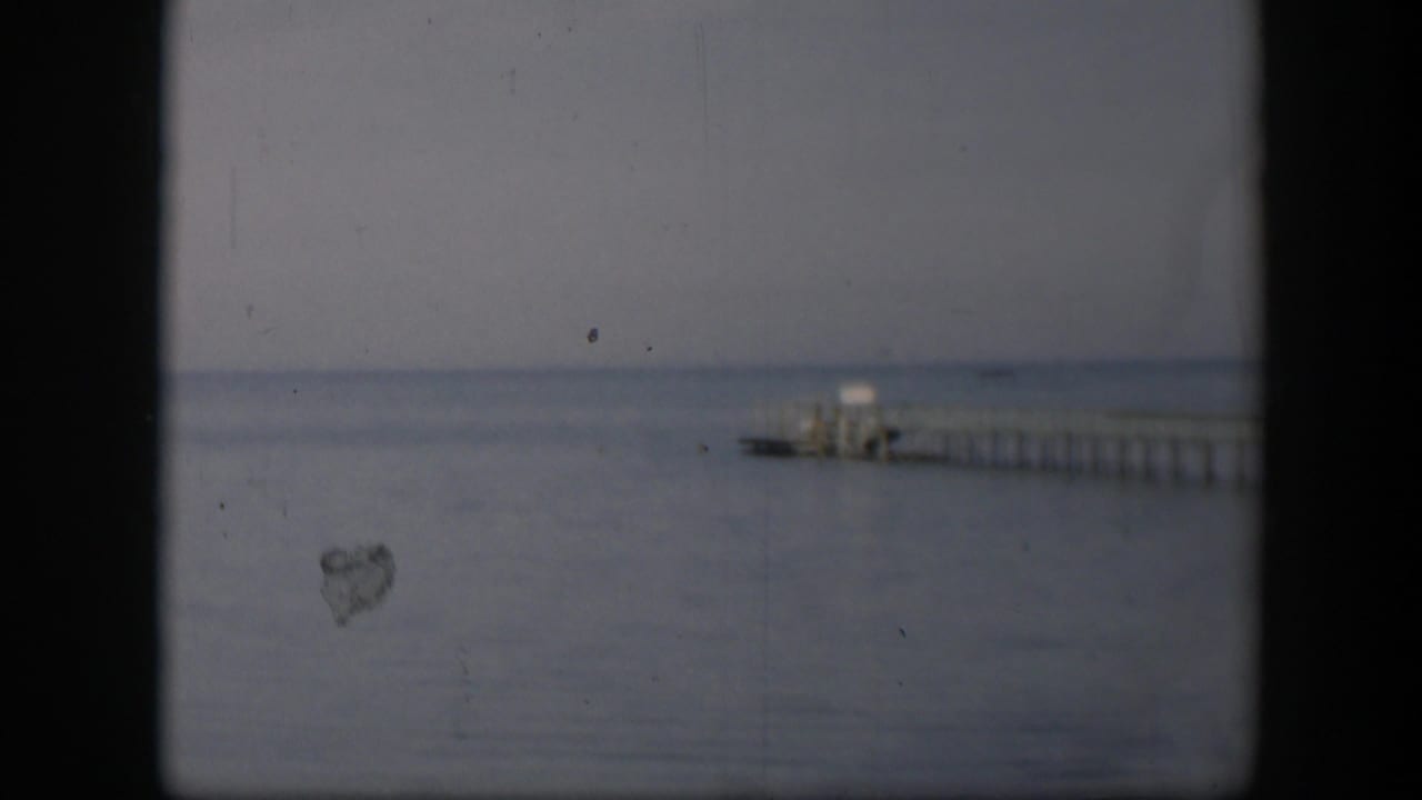 1951 Utah 8mm frame showing a distant wooden pier over calm water beneath a flat, overcast sky.