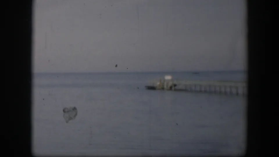 1951 Utah 8mm frame showing a distant wooden pier over calm water beneath a flat, overcast sky.