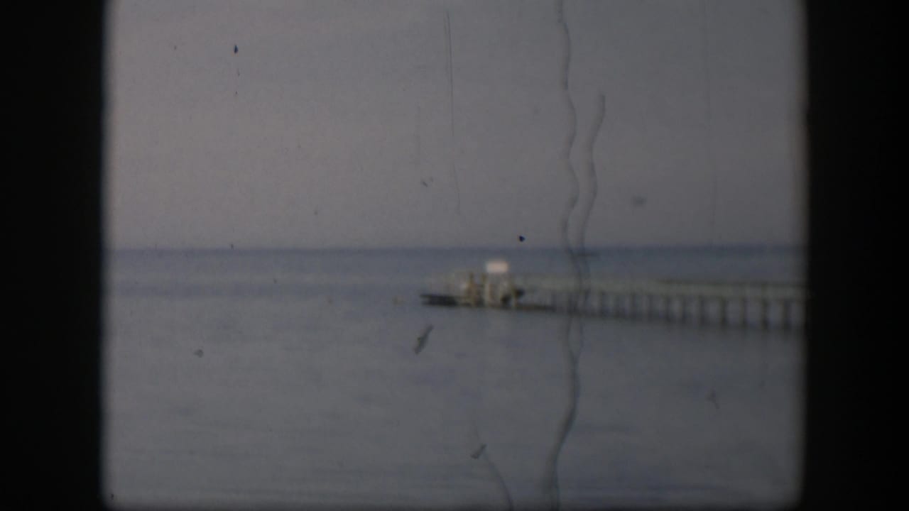 Soft 8mm view of a long pier and small pale structure on a Utah waterfront in 1951, framed by visible scan borders.