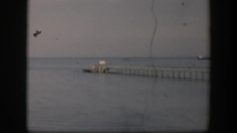 1951 Utah 8mm frame showing a wooden dock over calm water, a small moored boat, hazy horizon, and visible film edges.